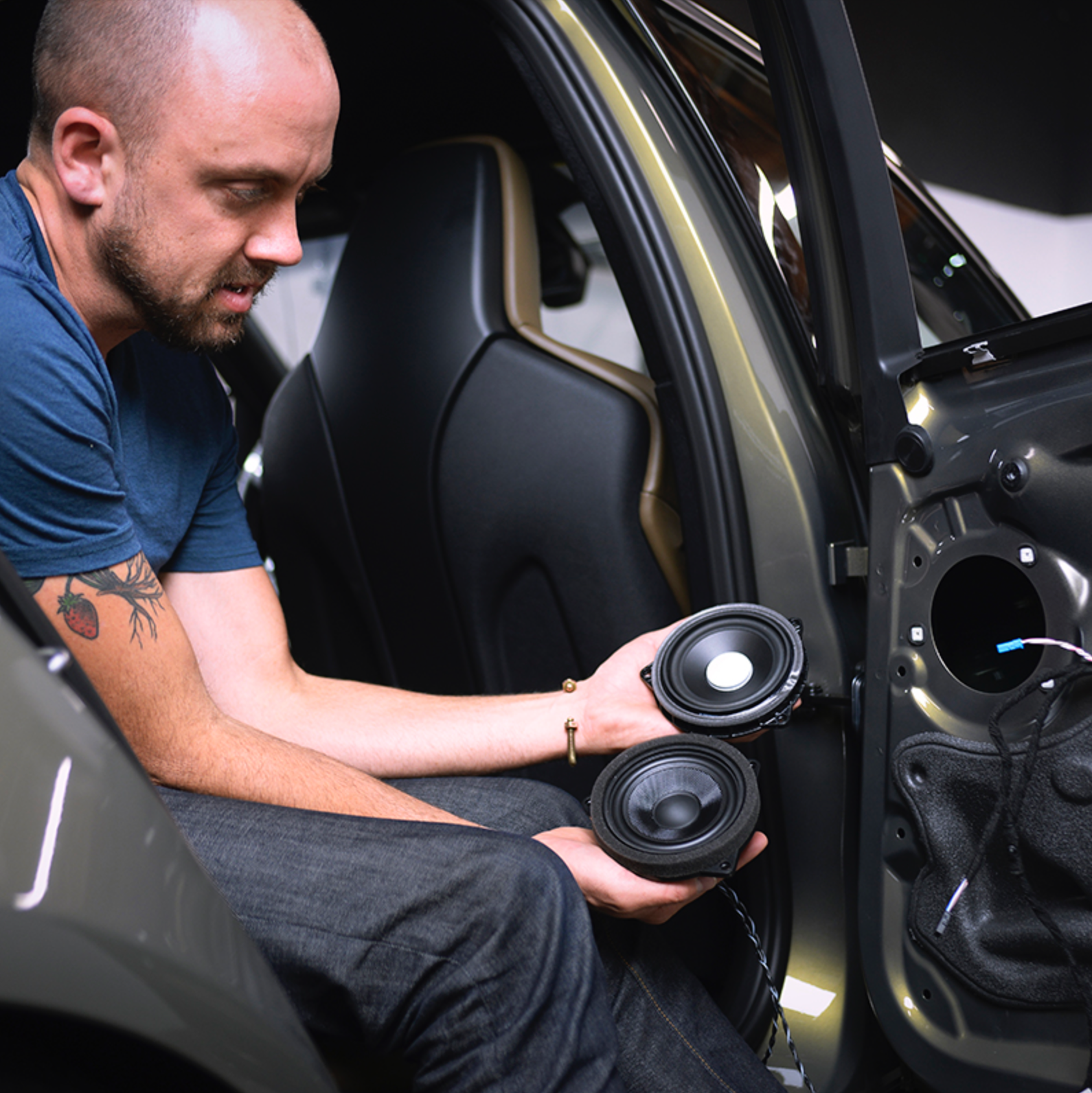 Man holding a Bavsound mid-range speaker next to a factory speaker showing the increase in build quality and materials.